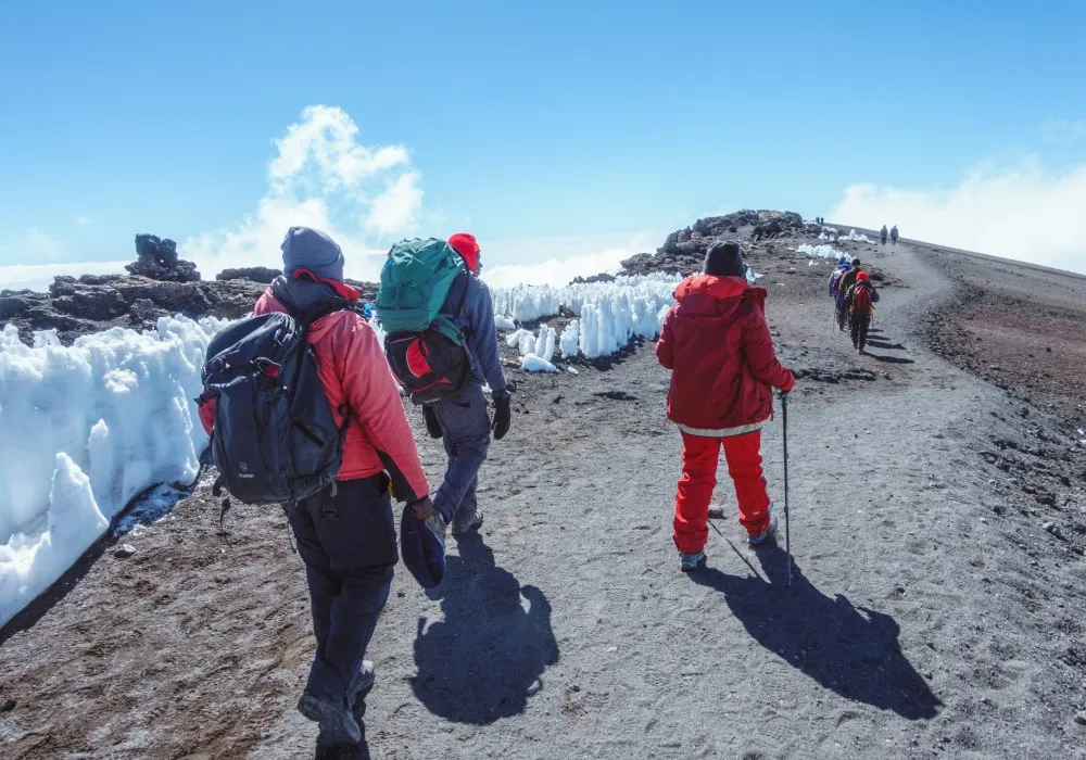Hikers walking beside ice on Mount Kilimanjaro's crater rim